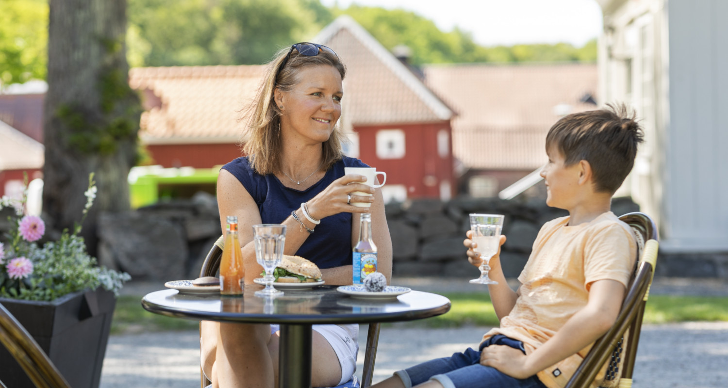 Mor och son med fika vid cafébord utomhus.