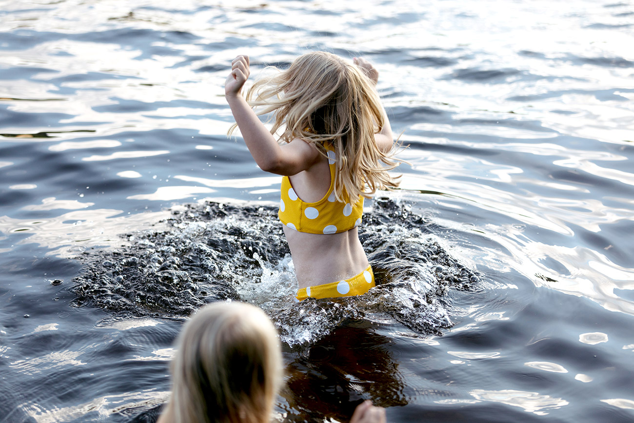 Flicka med prickig bikini hoppar runt i vattnet.