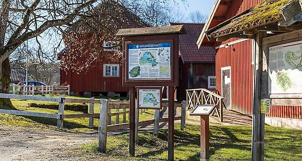 Skylt med kartvy över naturreservatet vid Rådasjön, framför röda stallbyggnader.